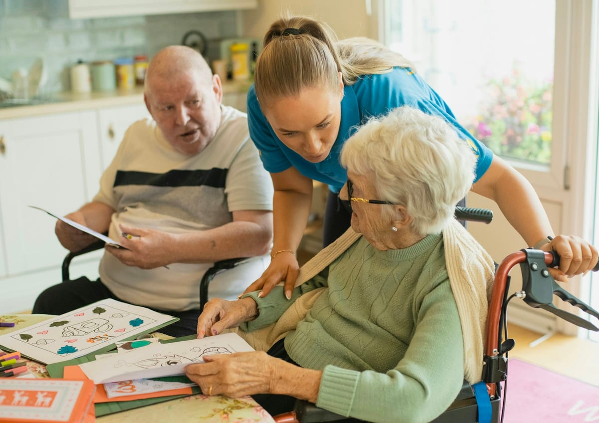 A caregiver helping two older adults with an activity at a kitchen table
