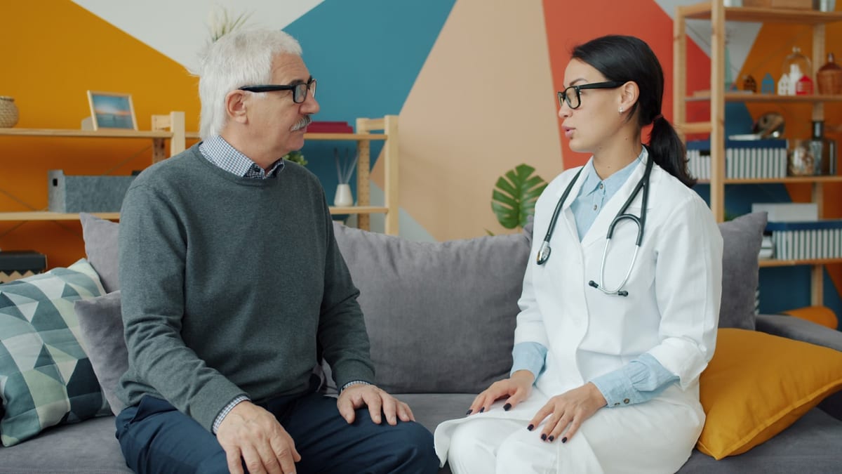 A care professional talking with an older man in his living room during a home visit